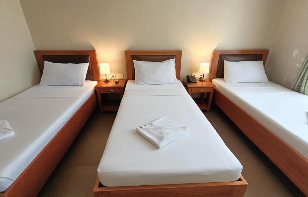 A hotel room with three single beds, each with a wooden headboard and white bedding.