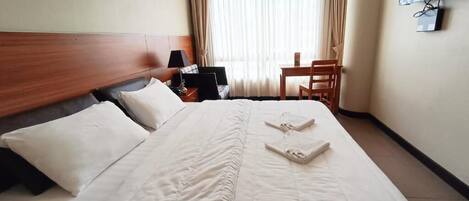 A hotel room with a large bed, a desk, a chair, a TV, and a window with curtains.