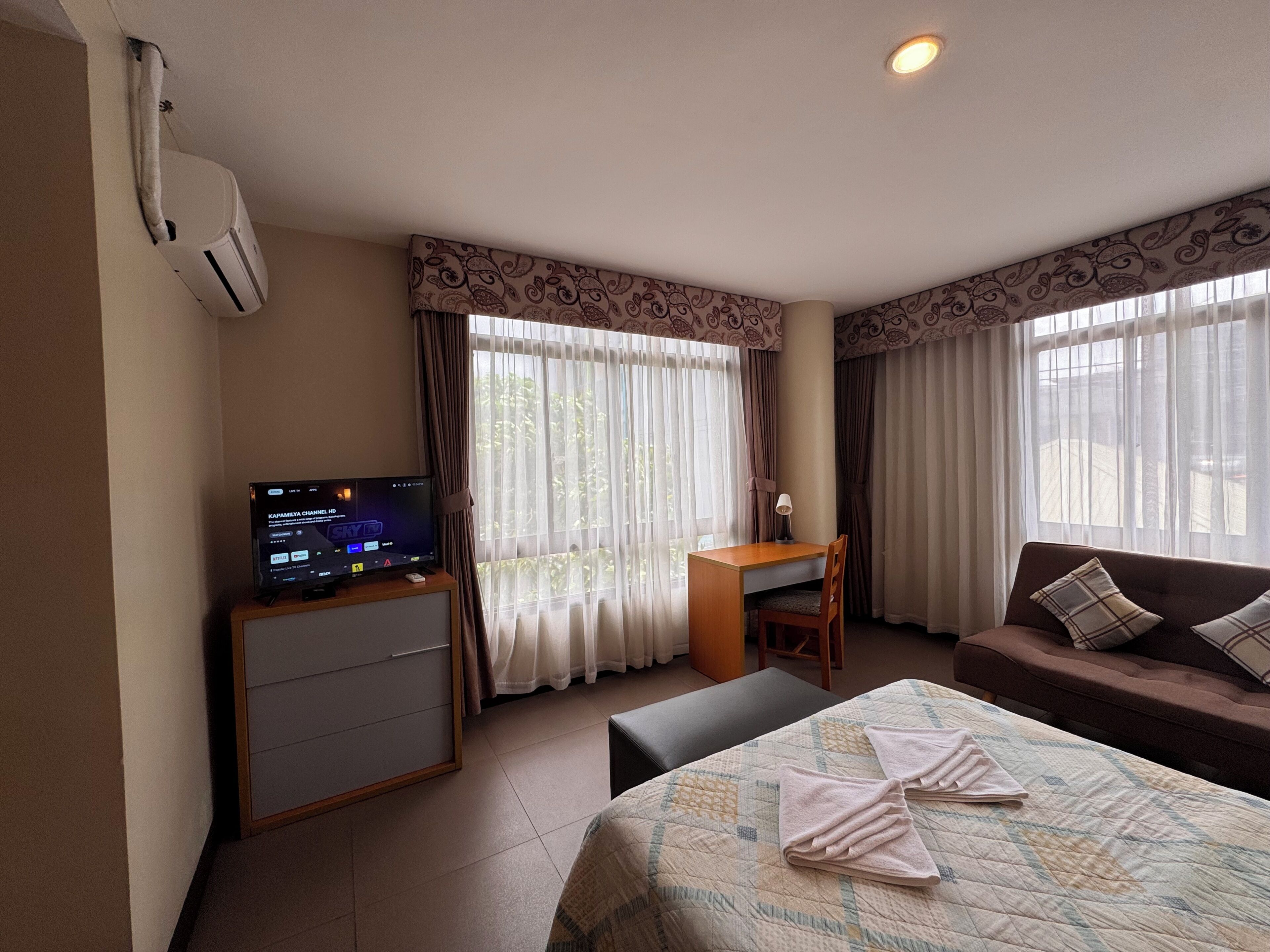 A hotel room with a bed, a desk, a chair, a couch, and a television.