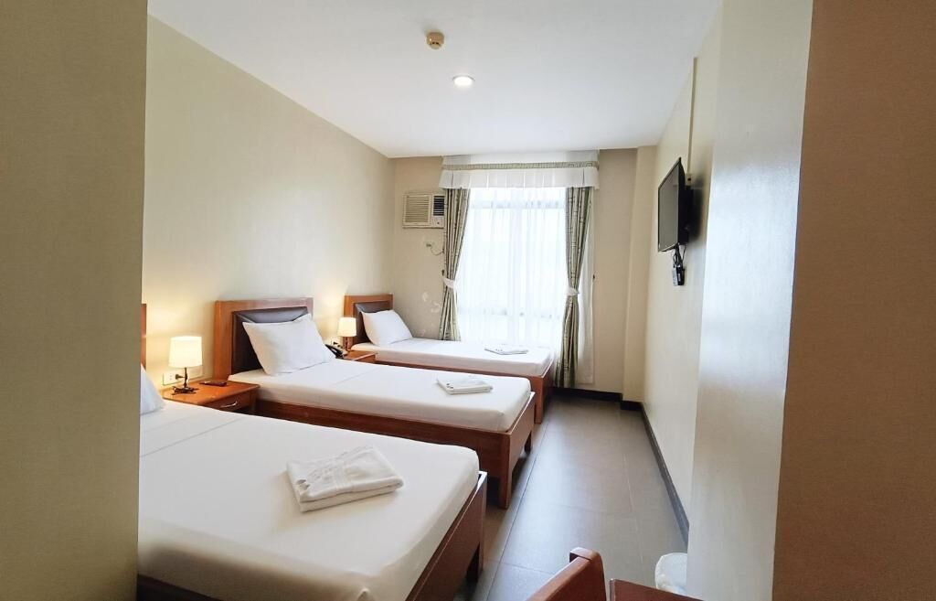 A hotel room with two single beds, a TV mounted on the wall, and a window with curtains.