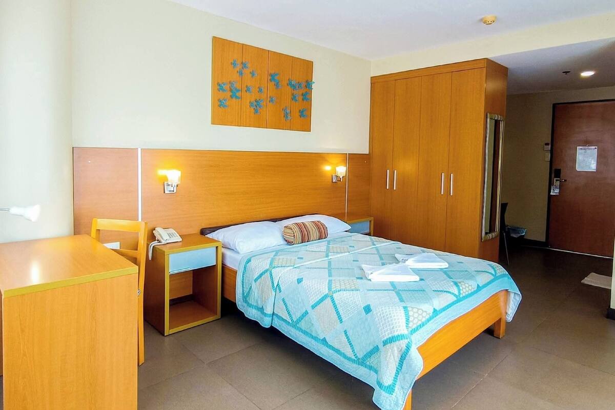 Habitación de hotel con cama, escritorio, silla, armario y una obra de arte en la pared.