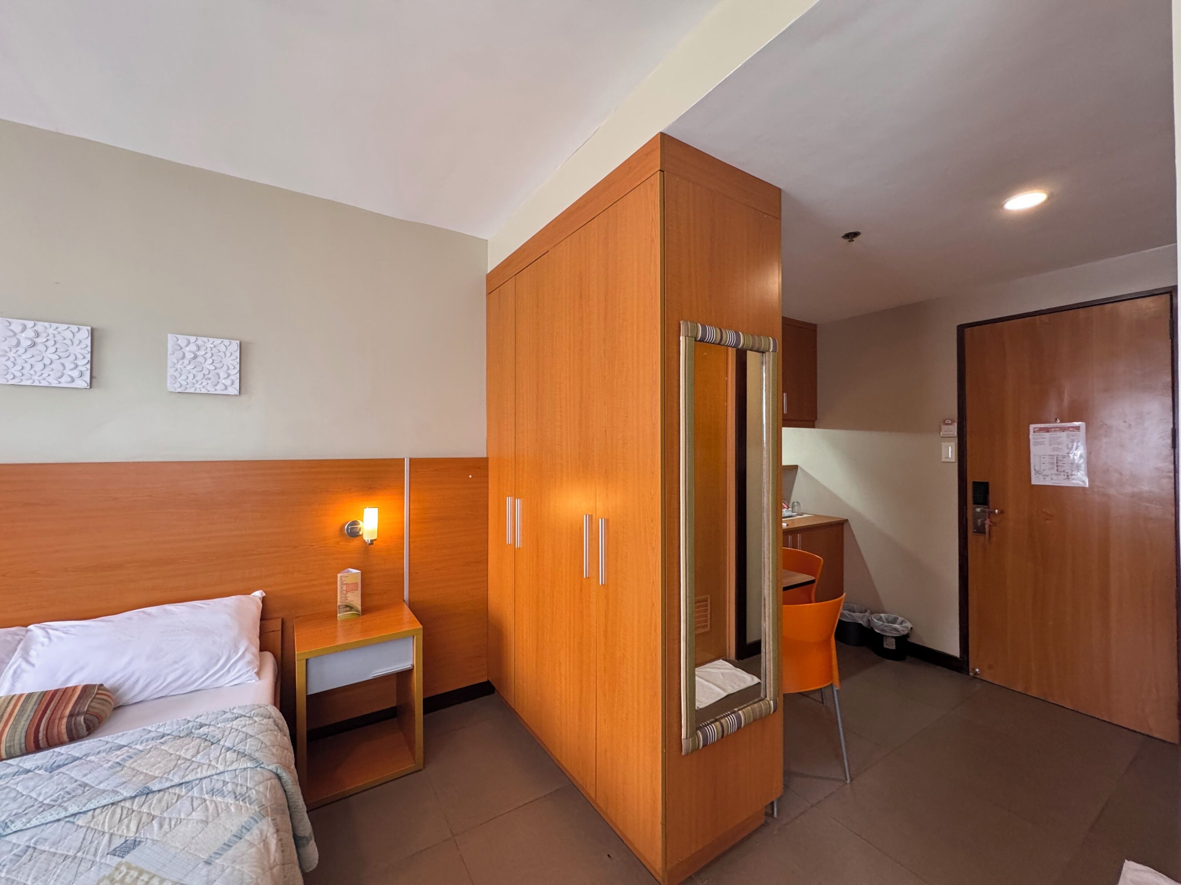 Une chambre d’hôtel comprenant un lit, une armoire en bois, une petite table de chevet, une chaise et un bureau.