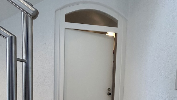 A hallway with a white door, a metal handrail, and a tiled floor. - Cozy vacation apartment with balcony - 2 bedrooms with 2 private bathrooms (Erden)