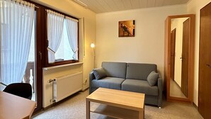 A living room with a sofa, a table, a radiator, and a window with curtains. - Cozy vacation apartment with balcony - 2 bedrooms with 2 private bathrooms (Erden)