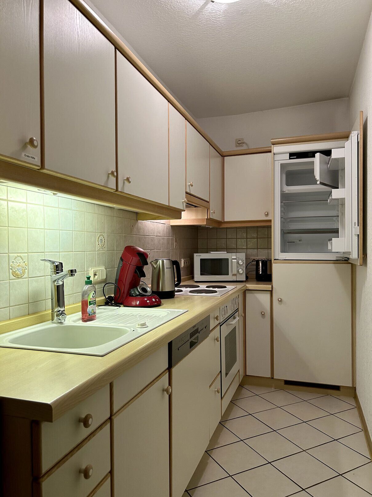 Eine kleine Küche mit Spüle, Herd, Mikrowelle und Kühlschrank.