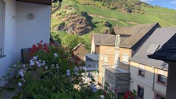 Ein Wohngebiet mit terrassenförmig angelegten Weinbergen im Hintergrund, ein weißes Gebäude mit Balkon und ein abgestelltes Auto.