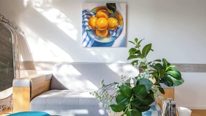 Un soggiorno moderno con un divano, un tavolino da caffè, una pianta decorativa e un quadro raffigurante della frutta appesa alla parete.