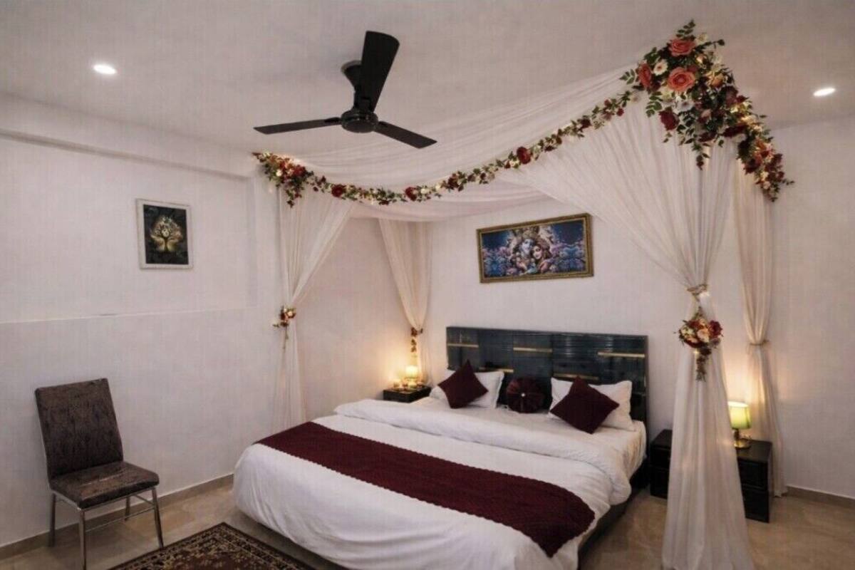 Un dormitorio con cama, ventilador de techo, una silla y mesita de noche con lámpara.