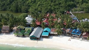 Vista aérea de un resort frente a la playa con varias cabañas tipo bungalow, palmeras y una vista despejada del océano.