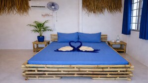 Una cama con colcha azul, dos almohadas azules, una toalla dispuesta en forma de corazón, una planta en maceta y una alfombra con diseño azul y blanco.