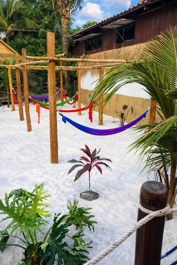 Uma estrutura de madeira com cordas e uma rede, cercada por vegetação e um edifício com telhado de palha.