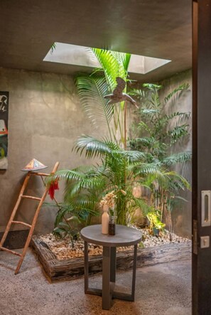 A room with a concrete wall, a small table with a bottle, a ladder, and a large plant. - “Exclusive 3-Bedroom Villa – Perfect for Shared Living with Family” (Tibubeneng)