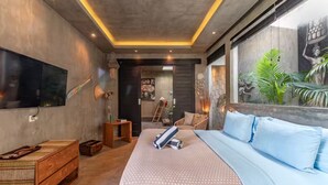 Een moderne slaapkamer met een groot bed, een televisie, een houten kist en een raam met uitzicht op groen.