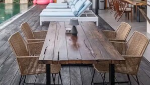 Een houten terras met een eettafel en stoelen, een zwembad, ligbedden, en een moderne keuken zichtbaar door een geopende deur.