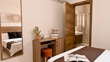 A hotel room with a bed, a desk with a plant, a mirror, and a shower area.