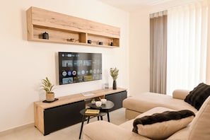 A modern living room with a flat-screen TV, wooden shelves, a small table with a plant, and a sofa. - Viviani Court 2bd Modern Apt Xewkija Gozo (Xewkija)