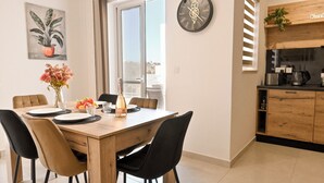 A dining area with a wooden table, black chairs, a vase with flowers, and a city view through a sliding door. - Viviani Court 2bd Modern Apt Xewkija Gozo (Xewkija)