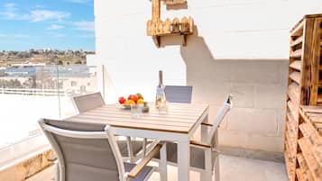 Un balcone con tavolo e sedie in legno e una ciotola di frutta.