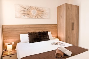 Un dormitorio con cabecera de madera, un cuadro abstracto grande, un armario, una mesita de noche con lámpara y una toalla enrollada.