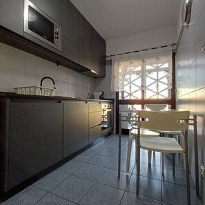A modern kitchen with a microwave, cabinets, a sink, and a chair. - Stay in Porto in an Authentic Neighborhood (Oporto)