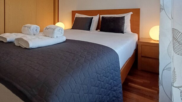 A hotel room with a bed, pillows, a nightstand, and towels. - Stay in Porto in an Authentic Neighborhood (Oporto)