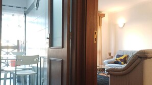A room with a wooden door, a glass table with chairs, a sofa, and a wall-mounted clock. - Stay in Porto in an Authentic Neighborhood (Oporto)