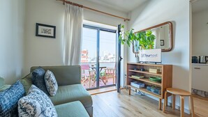 A living room with a sofa, a small table, a bookshelf, a potted plant, and a sliding glass door leading to an outdoor area. - Charming retreat near Boavista with elevator (Oporto)
