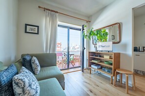 Un salon comprenant un canapé, une petite table, une bibliothèque, une plante en pot et une porte-fenêtre coulissante donnant sur un espace extérieur.