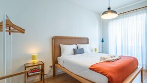 A single bed with a wooden headboard, a bedside table with a lamp, and a window with sheer curtains. - Charming retreat near Boavista with elevator (Oporto)
