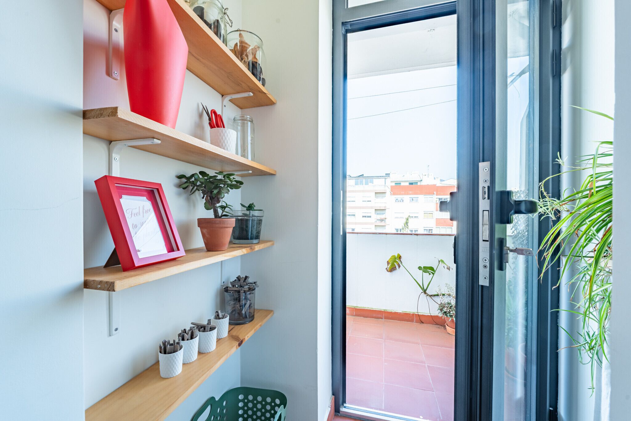 Une pièce dotée d’une porte-fenêtre coulissante donnant sur un balcon, d’étagères remplies de divers objets et d’un fauteuil vert.