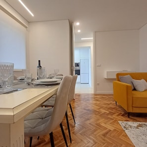 A modern living room with a dining area, a yellow sofa, and a kitchen in the background. - Porto Luxury Downtown Apartment & Garage (Oporto)