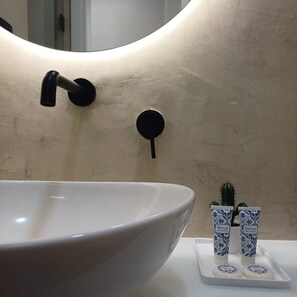 A bathroom with a large white sink, a mirror with a curved frame, and two small blue and white patterned containers on a tray. - Porto Luxury Downtown Apartment & Garage (Oporto)