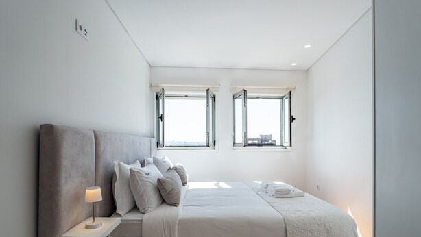 A bedroom with a bed, bedside table, lamp, and two windows. - Porto Luxury Downtown Apartment & Garage (Oporto)