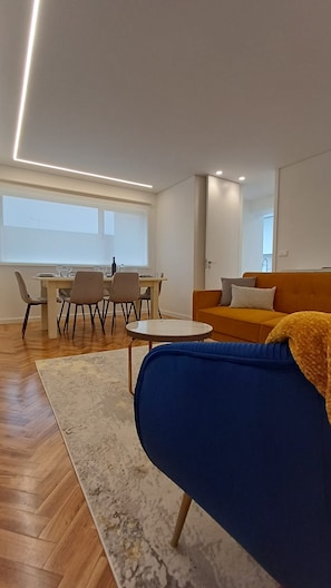 A modern living room with a sofa, a dining table with chairs, and a large window. - Porto Luxury Downtown Apartment & Garage (Oporto)