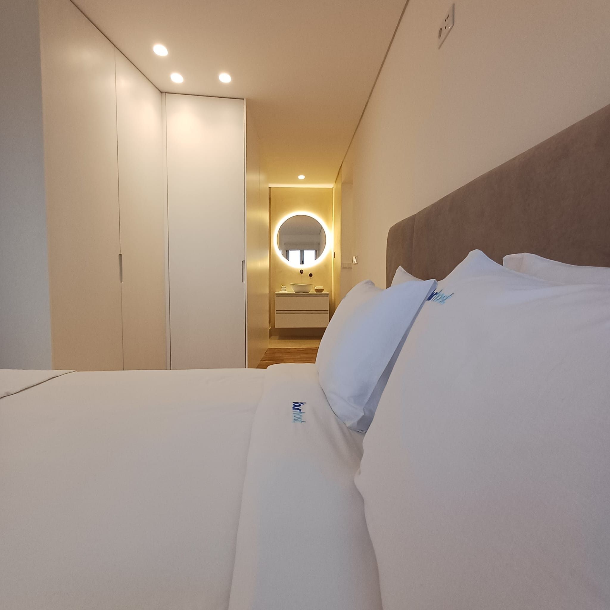 A hotel room with a bed, a bedside table, a mirror, and a bathroom visible through an open door.