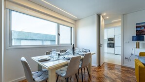 A modern dining area with a wooden table, four chairs, and a view through a large window. - Porto Luxury Downtown Apartment & Garage (Oporto)