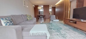 Ein modernes Wohnzimmer mit einer Couch, einem Fernseher, einem Esstisch und einem Sessel.