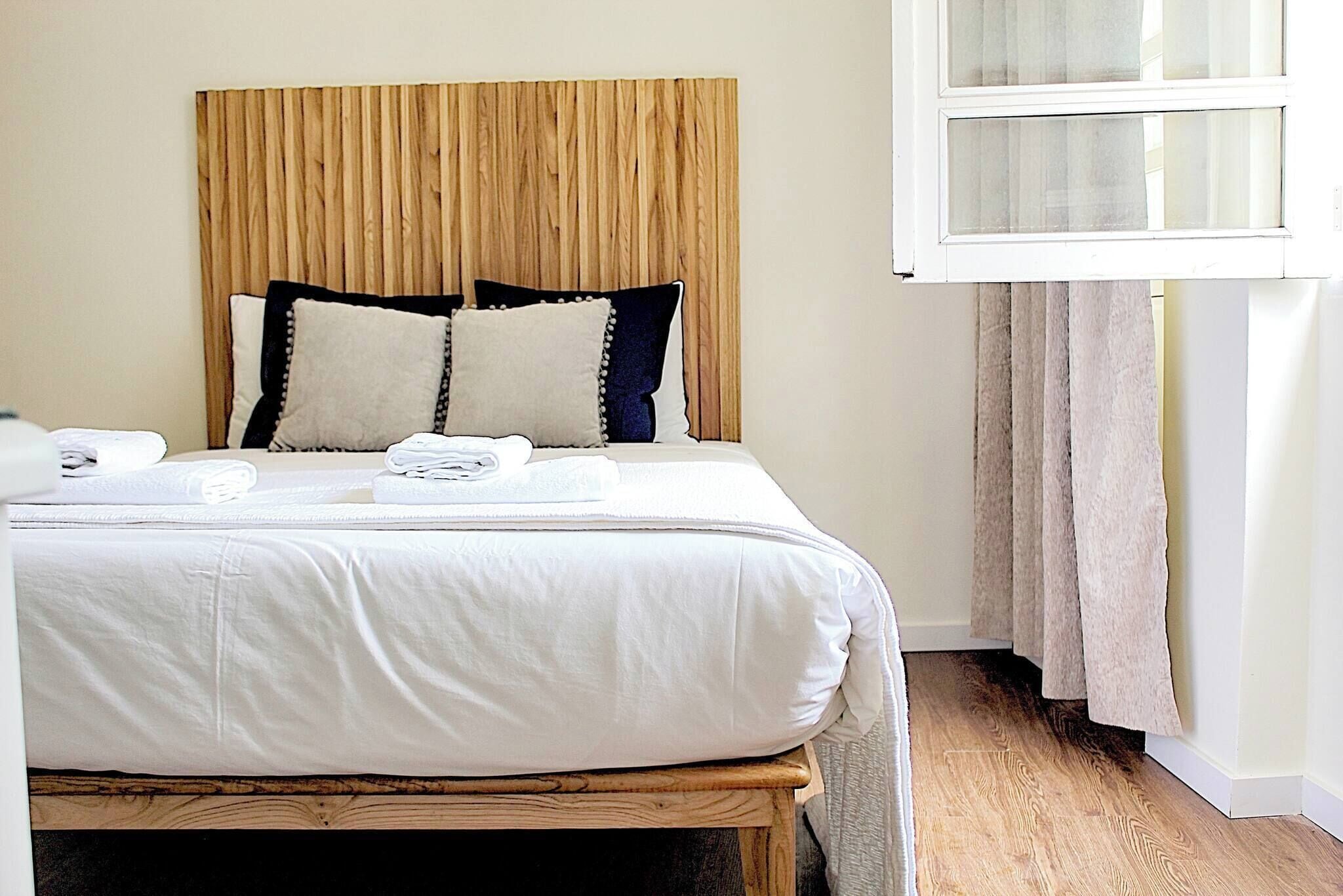 Ein Bett mit Holz-Kopfstück, weißer Bettwäsche und zwei Kissen.