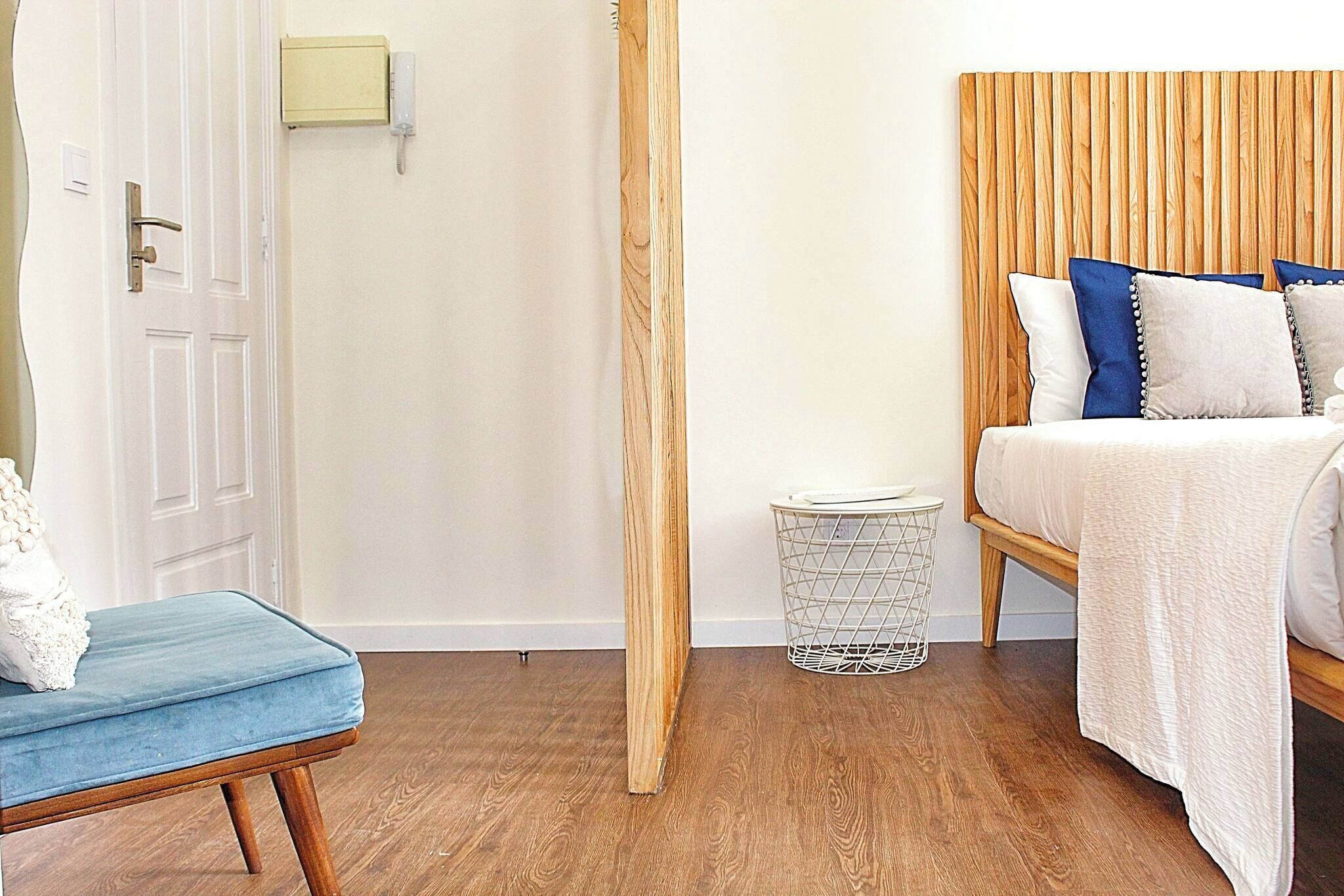A bedroom with a wooden headboard, a bed with white bedding, a blue chair, and a white door.