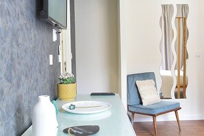 Ein modernes Wohnzimmer mit einem Glastisch, einem blauen Sessel, einer gelben, gemusterten Vase und einem wandmontierten Flachbildfernseher.