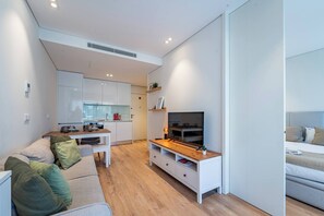 A modern living room with a sofa, TV stand, and a kitchen in the background. - Antas Park Concept Lifestyle With Pool (Oporto)