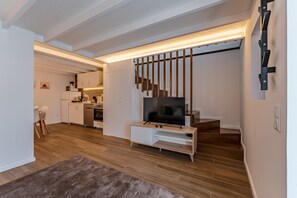 Una sala de estar moderna con un televisor de pantalla plana, piso de madera y una escalera que sube a un nivel superior.