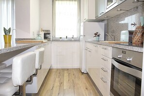 Eine moderne Küche mit weißen Schränken, Holzboden, integriertem Backofen und einem Fenster mit Vorhängen.