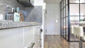A modern kitchen with granite countertops, stainless steel appliances, and a view into a dining area with a wooden floor. - Arrábida Luxury Studio (Vila Nova de Gaia)