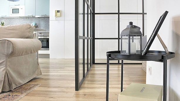 A modern living room with a sofa, a black metal table with a lantern, and a kitchen in the background. - Arrábida Luxury Studio (Vila Nova de Gaia)
