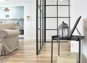 Un salon moderne avec un canapé, une table en métal noir surmontée d’une lanterne, et une cuisine en arrière-plan.