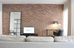 Ein Wohnzimmer mit Backsteinwand, einem großen Spiegel, einem Flachbildfernseher, einer modernen Stehlampe und einem Sofa.