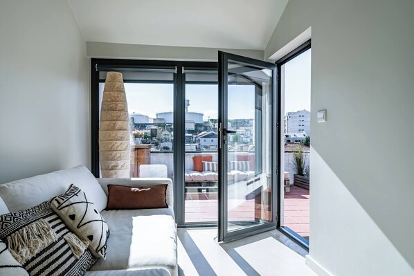 Ein modernes Wohnzimmer mit einer Couch, einem großen Fenster und Blick auf die Stadtlandschaft.