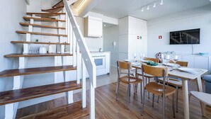 Una cocina moderna con armarios blancos, una zona de comedor con sillas de madera y una escalera con escalones de madera.