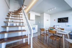 Eine moderne Küche mit weißen Schränken, ein Essbereich mit Holzsesseln und eine Treppe mit Holzstufen.